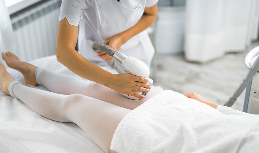 Technician performs Endermologie cellulite treatment on a patient's legs using a specialized device in a wellness clinic setting.