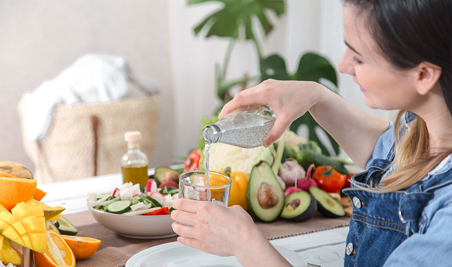A woman pouring chia seed water into a glass, surrounded by healthy fruits and vegetables, promoting wellness and vitality.