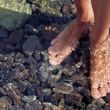 Bare feet standing in clear water over smooth stones, evoking tranquility and wellness.