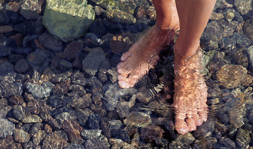 Bare feet standing in clear water over smooth stones, evoking tranquility and wellness.
