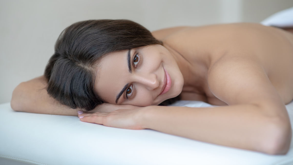 Smiling woman relaxing on a massage table, representing Pulsed Electromagnetic Field (PEMF) Therapy Near Me in a calming wellness setting
