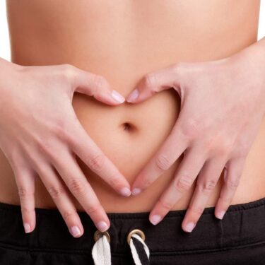 Hands forming a heart shape on a belly, symbolizing health and wellness.
