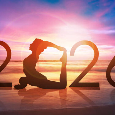 Silhouette of a person in a yoga pose at sunset on a beach, forming the number 2026 against a colorful sky.