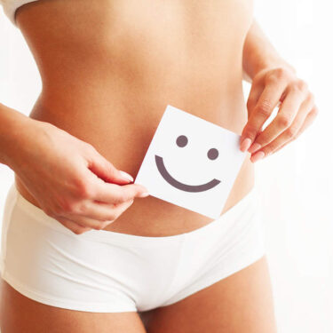 Person holding a smiley face card over their stomach, symbolizing health and wellness, in a bright setting.