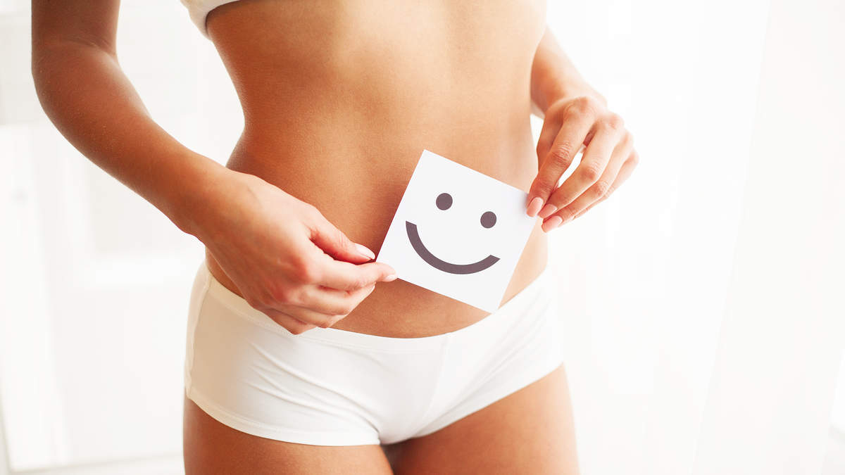 Person holding a smiley face card over their stomach, symbolizing health and wellness, in a bright setting.