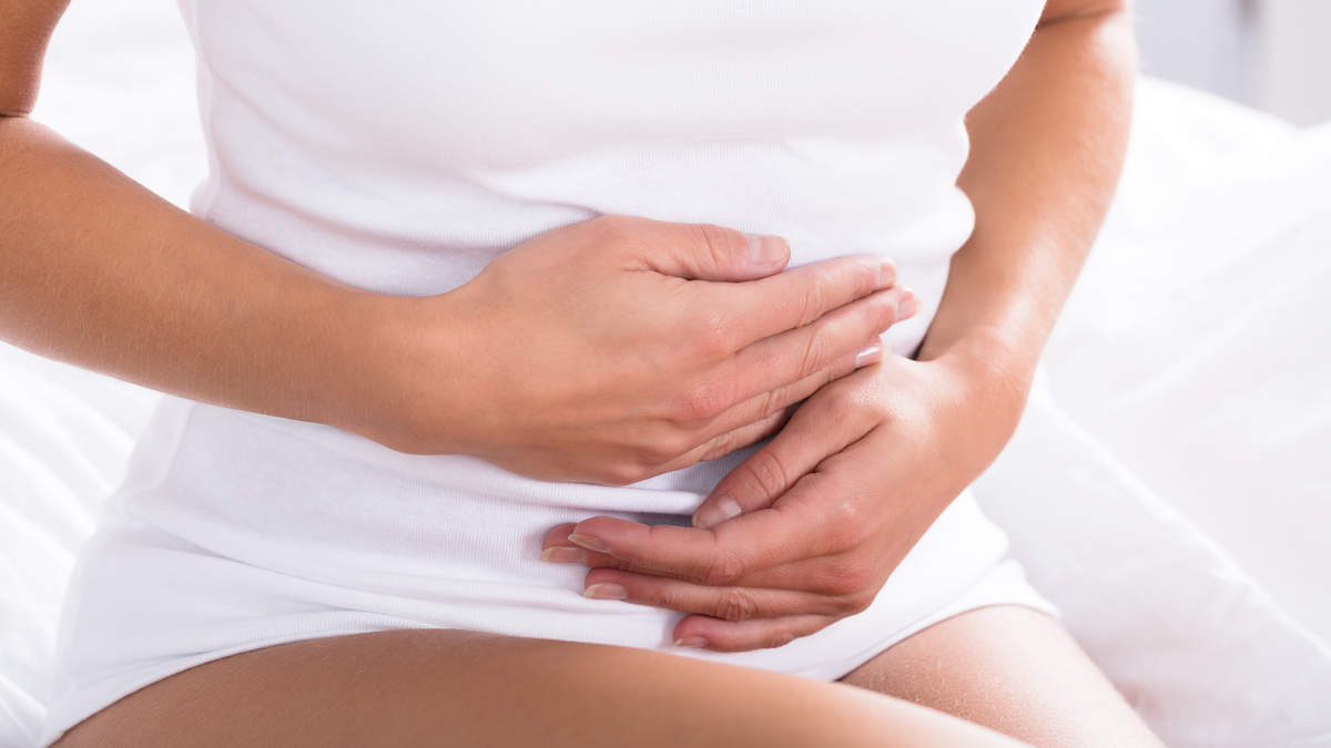 A person in a white tank top holds their stomach, conveying discomfort or digestive issues, relevant to health and wellness