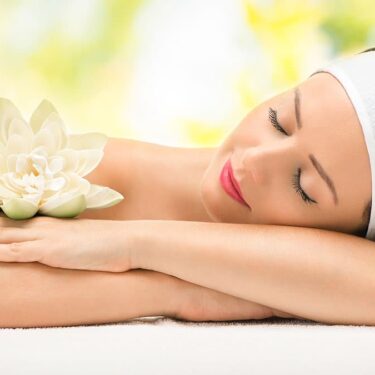 A serene woman resting with a white lotus flower on her shoulder, representing relaxation and wellness in a tranquil setting.