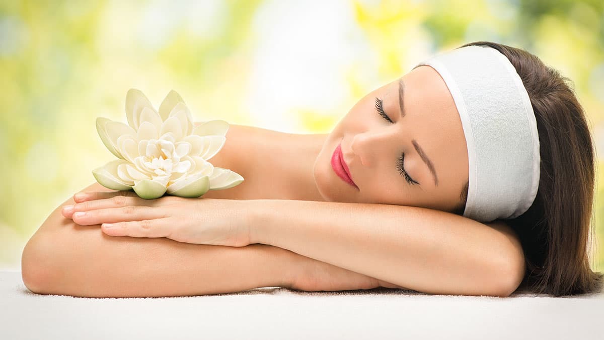 A serene woman resting with a white lotus flower on her shoulder, representing relaxation and wellness in a tranquil setting.