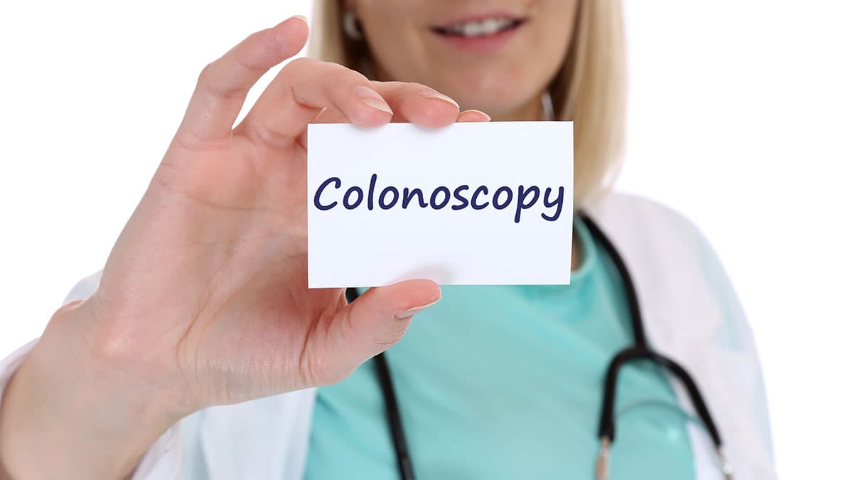 Healthcare professional holding a card that reads Colonoscopy, highlighting a service related to health and wellness.