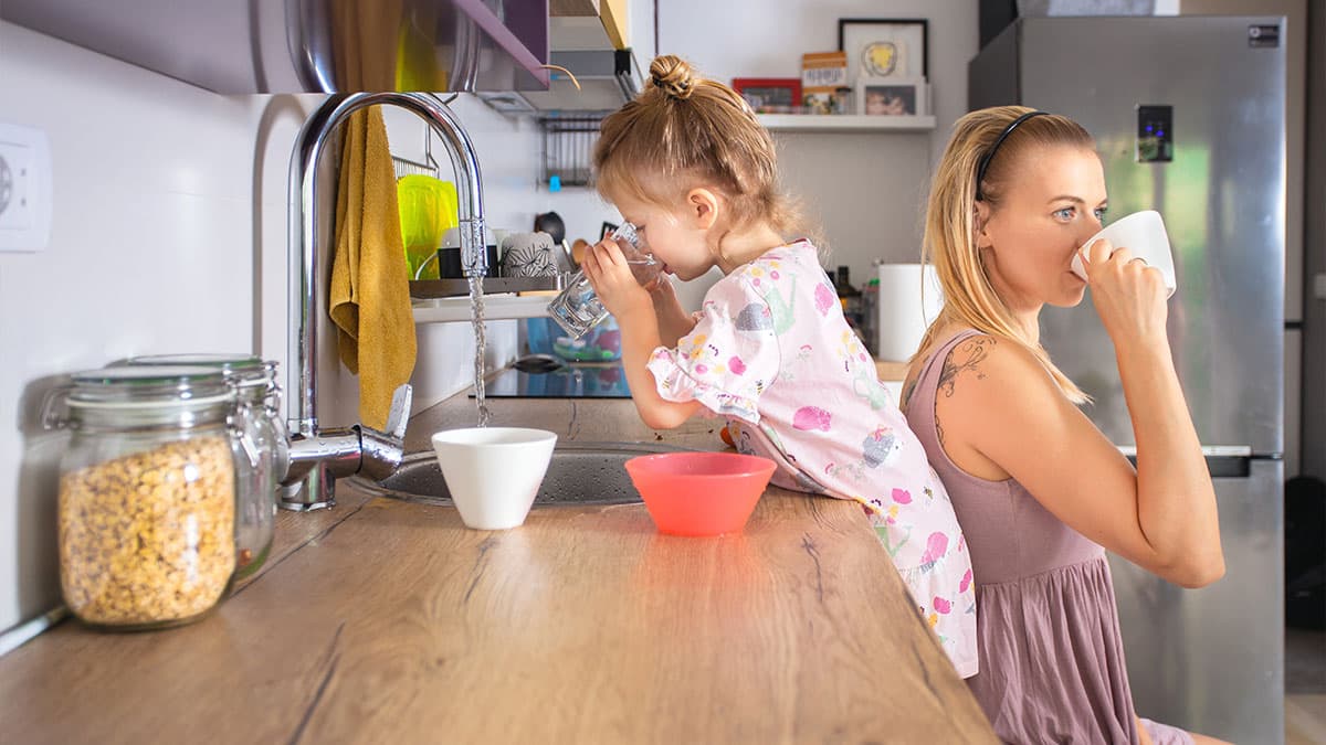 Postpartum mother drinking water with child nearby, showing hydration support during recovery after pregnancy