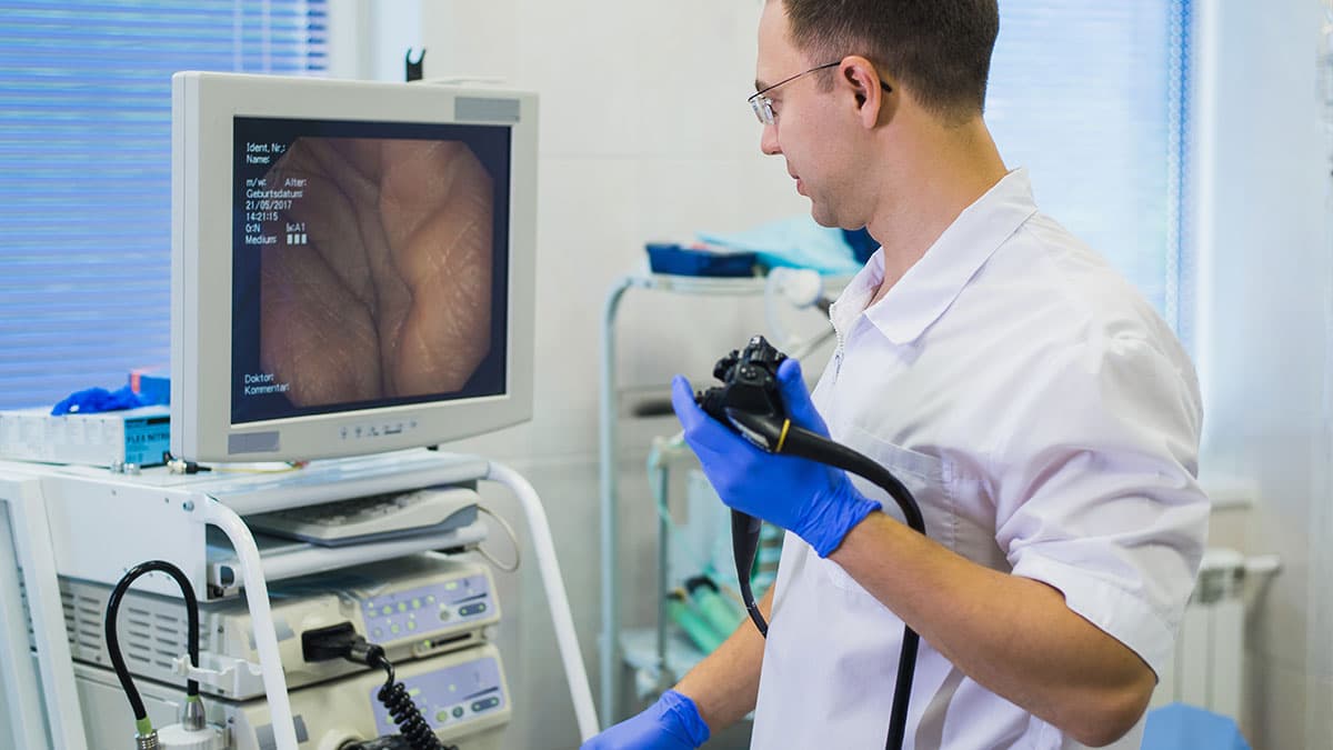 Healthcare professional holding an endoscope beside a monitor displaying the bowel lining during a colonoscopy.